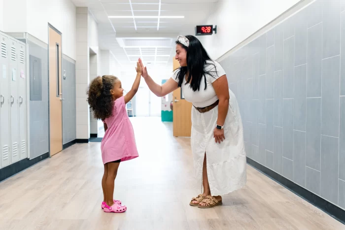 smiling teacher giving a high-five to a young Pre-K student in a bright Richardson ISD school hallway.