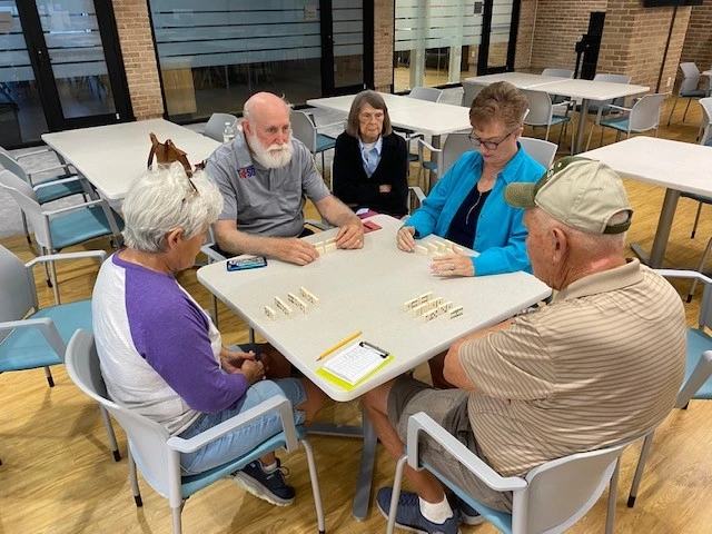 A group of four older adults sitting at a table together playing a game of dominoes.