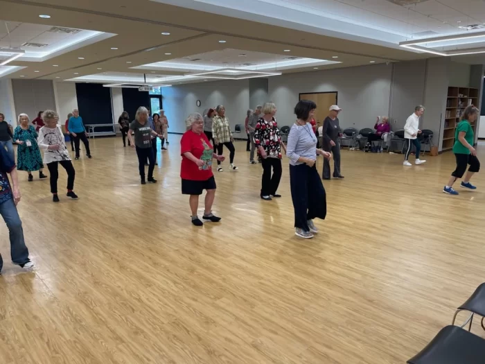 A large group of seniors participating in a choreographed line dancing class in a spacious hall at the Richardson Senior Center.