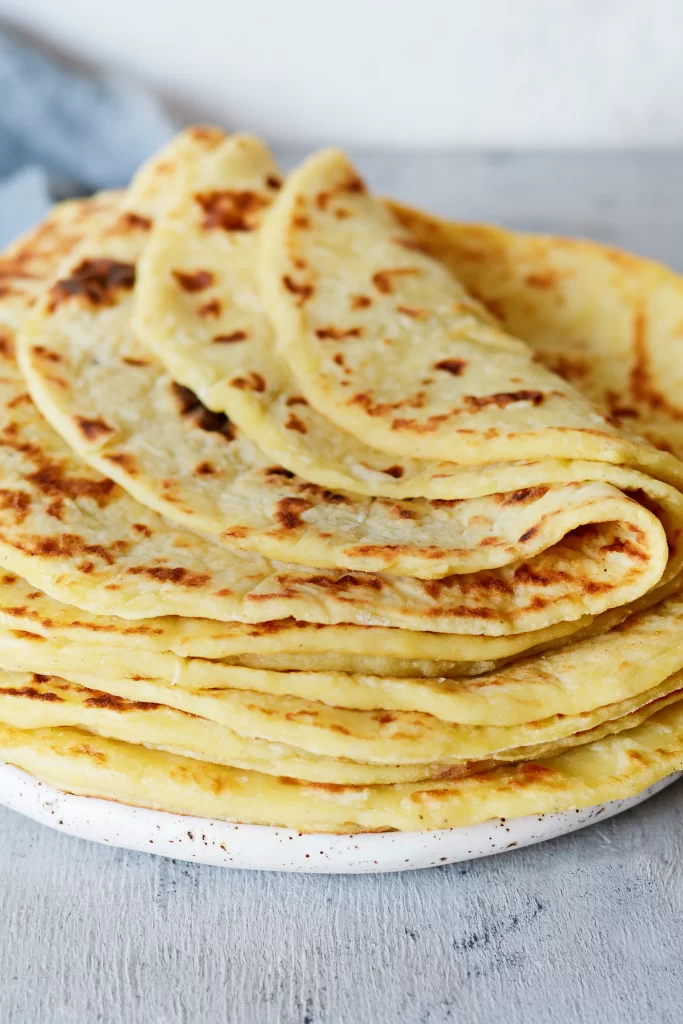 A stacked pile of freshly made Norwegian lefse, displaying a soft, folded potato flatbread with characteristic golden-brown spots.