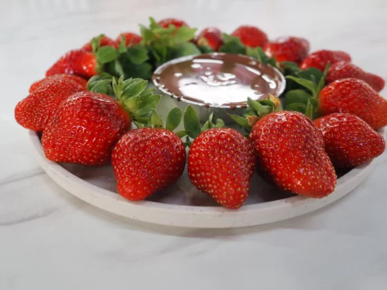 Bright red, juicy strawberries arranged in a circle on a white plate around a small foil container of melted dipping chocolate.