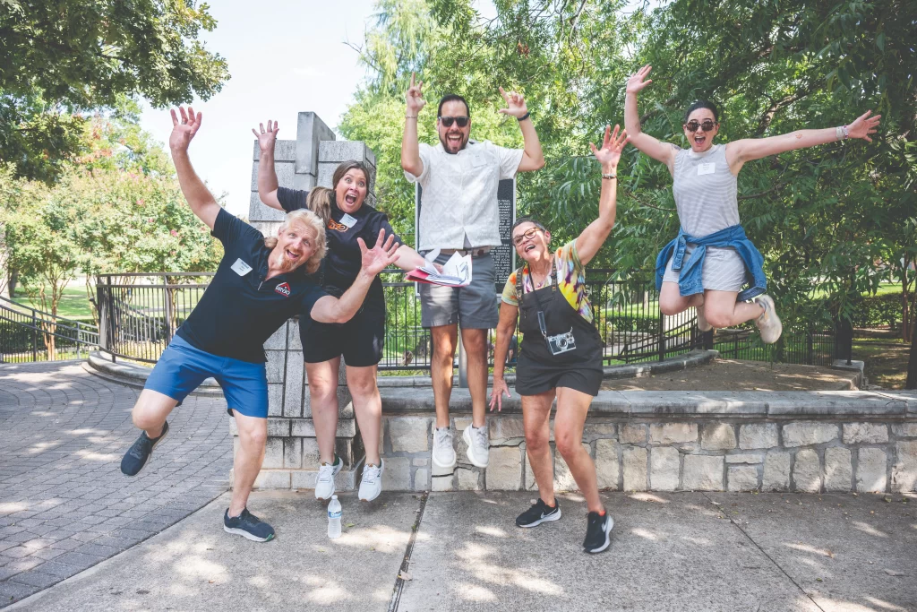 Group of participants jumping together along a shaded park walkway during an outdoor community event in Richardson.