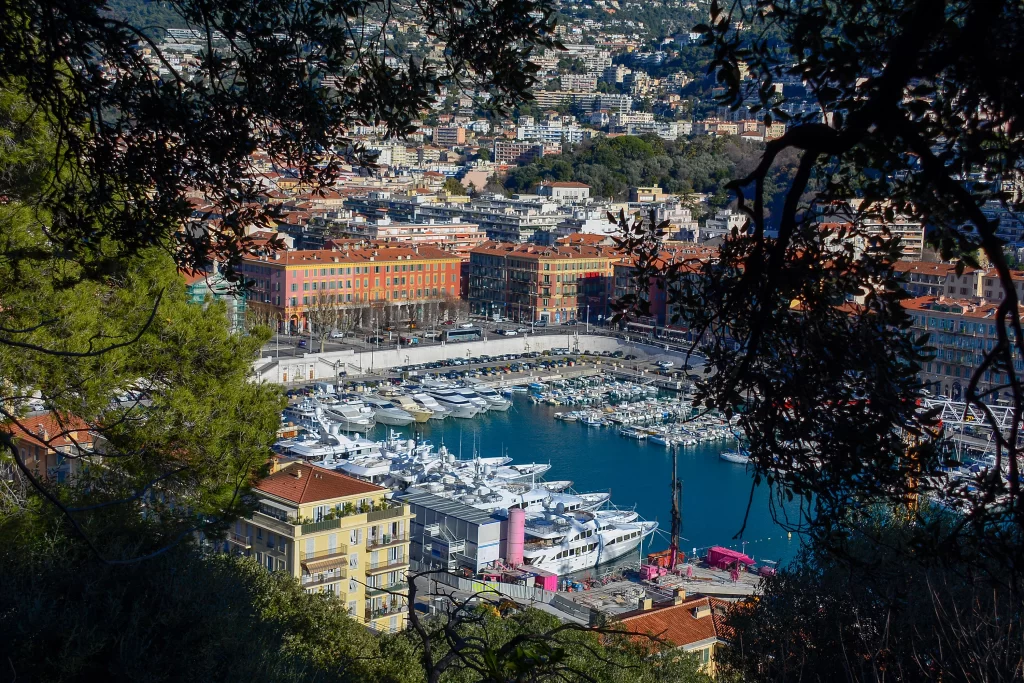 Elevated view of a Mediterranean marina and waterfront buildings along the Côte d’Azur framed by surrounding trees.