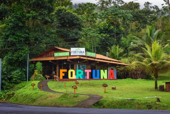 Colorful La Fortuna sign in front of a tourism information center surrounded by lush rainforest vegetation in Costa Rica.