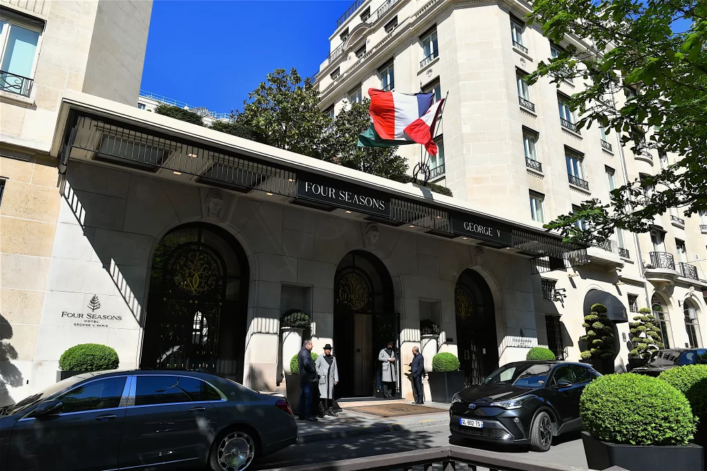 Exterior entrance of Four Seasons Hotel George V in Paris with French flags, manicured greenery, and luxury hotel façade.