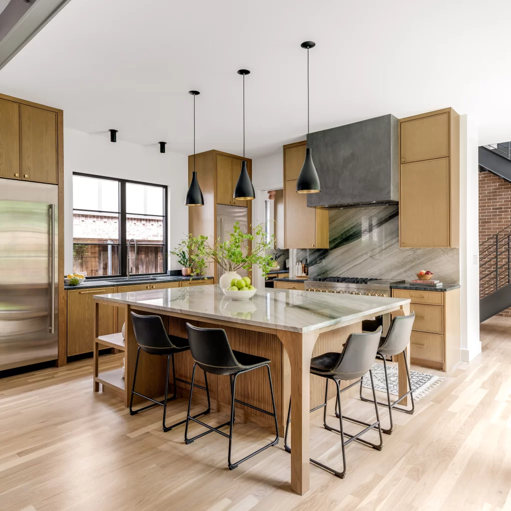 Contemporary kitchen with expansive island, wood cabinetry, large windows, and abundant natural light.