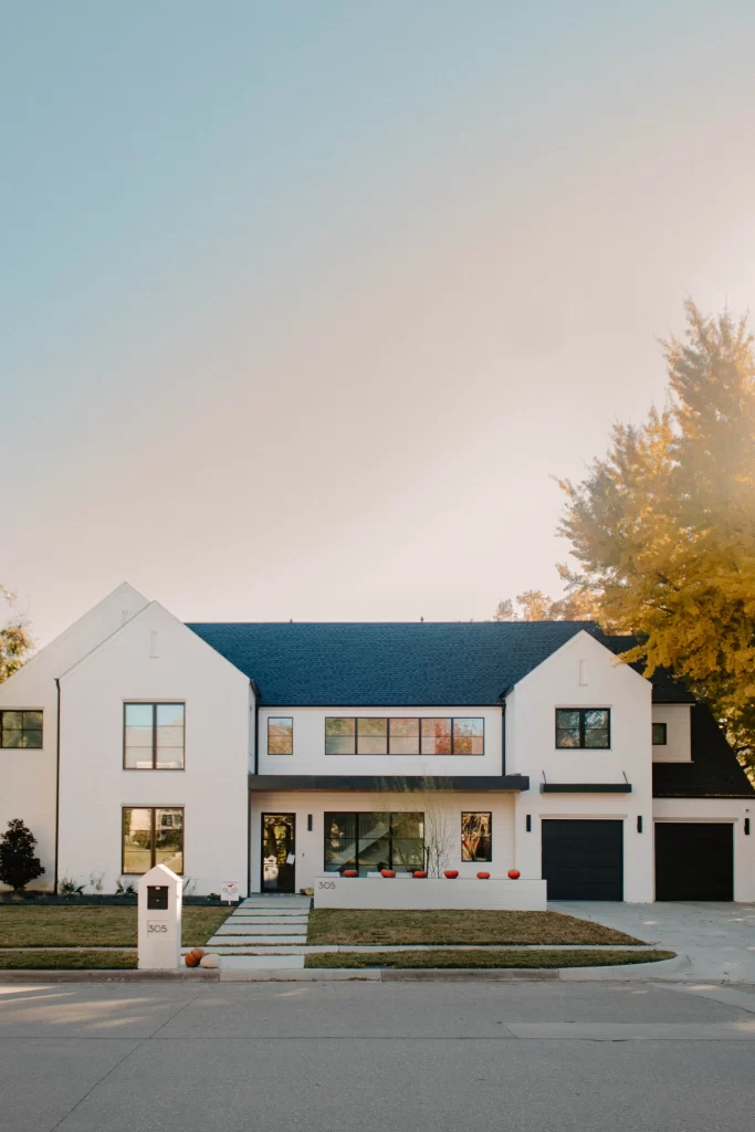 Modern white brick home with black roof, large windows, and landscaped front yard illuminated by natural daylight.
