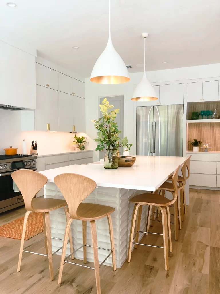 Bright contemporary kitchen with white island, wood seating, pendant lighting, and integrated cabinetry.